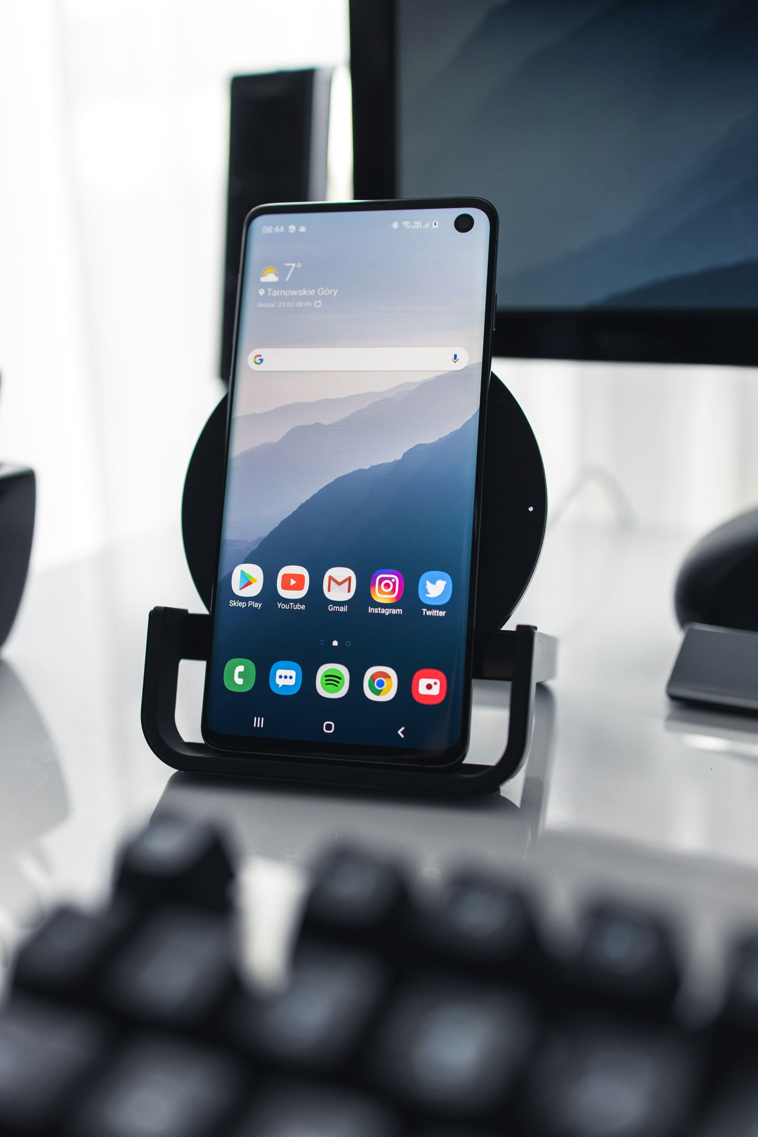 An affordable Android smartphone on a wooden desk showing its home screen